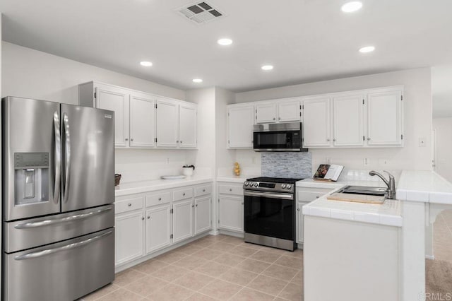 kitchen with a peninsula, appliances with stainless steel finishes, white cabinets, and a sink