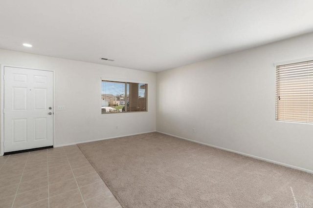 empty room featuring light carpet, light tile patterned floors, visible vents, baseboards, and recessed lighting