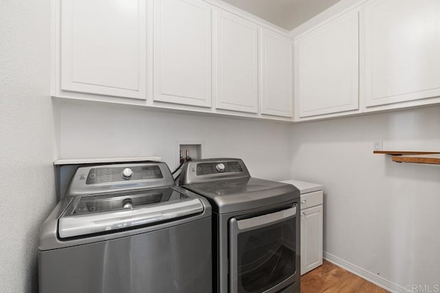 laundry area with baseboards, cabinet space, washer and clothes dryer, and light wood finished floors