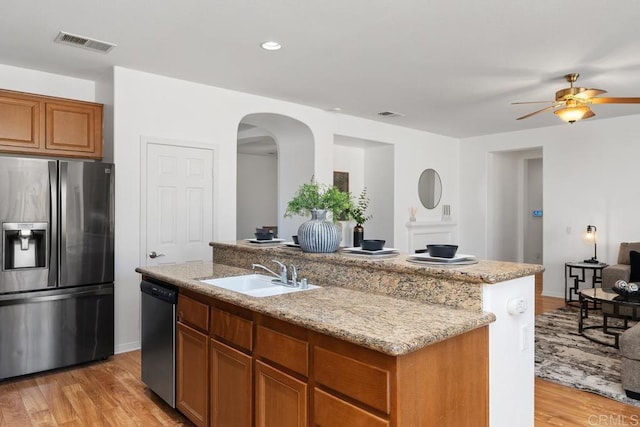 kitchen with brown cabinets, visible vents, appliances with stainless steel finishes, a sink, and an island with sink