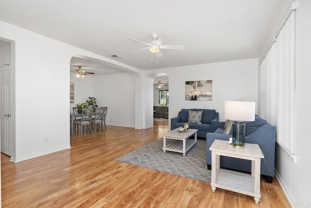 living room with a ceiling fan, arched walkways, visible vents, and wood finished floors