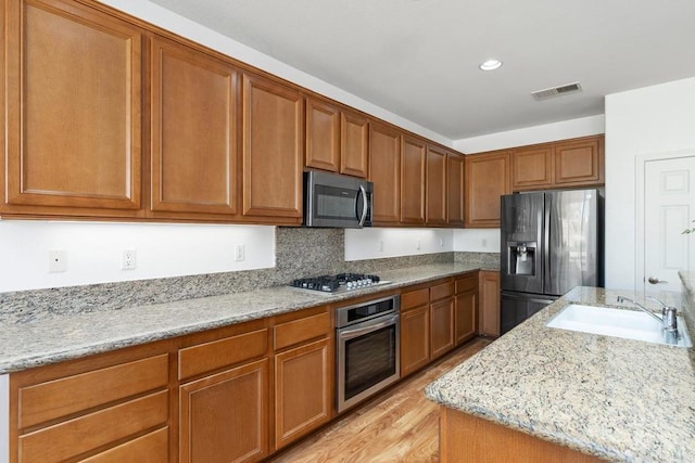 kitchen featuring stainless steel appliances, brown cabinetry, visible vents, and light stone counters