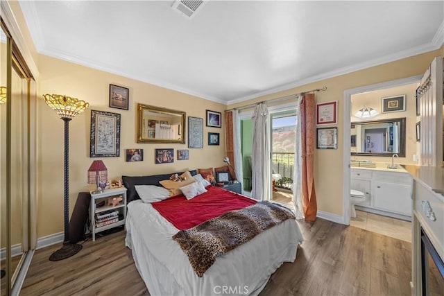 bedroom with connected bathroom, a sink, wood finished floors, visible vents, and access to exterior