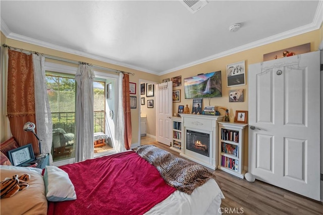 bedroom with wood finished floors, a glass covered fireplace, visible vents, and crown molding