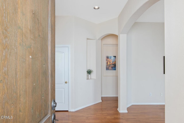 corridor with baseboards, arched walkways, wood finished floors, and recessed lighting