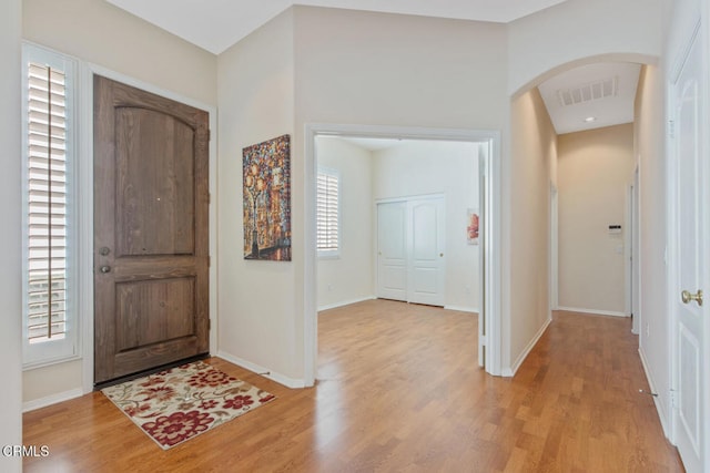 entrance foyer with light wood-style floors, baseboards, visible vents, and arched walkways