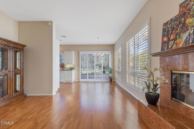 unfurnished living room featuring a chandelier, visible vents, baseboards, a high end fireplace, and light wood-style floors