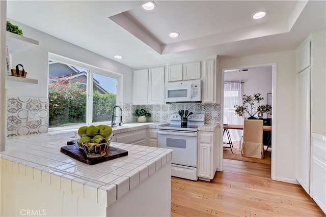 kitchen with tile countertops, white appliances, a tray ceiling, and white cabinets