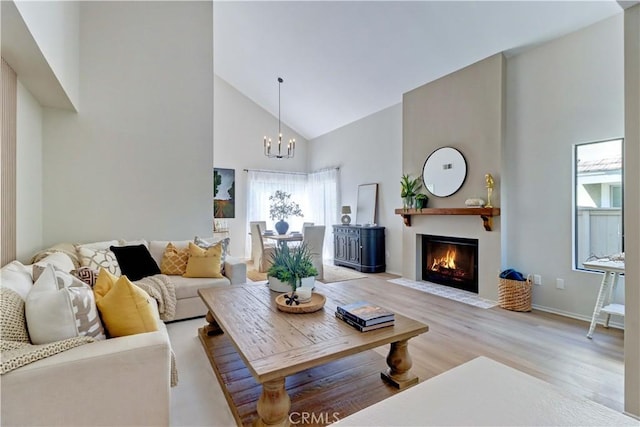 living room with a fireplace with flush hearth, high vaulted ceiling, light wood finished floors, and an inviting chandelier