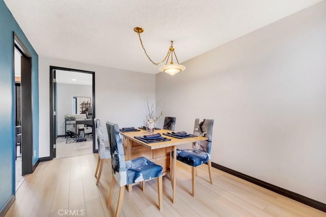 dining space with light wood-style floors, baseboards, and a textured ceiling