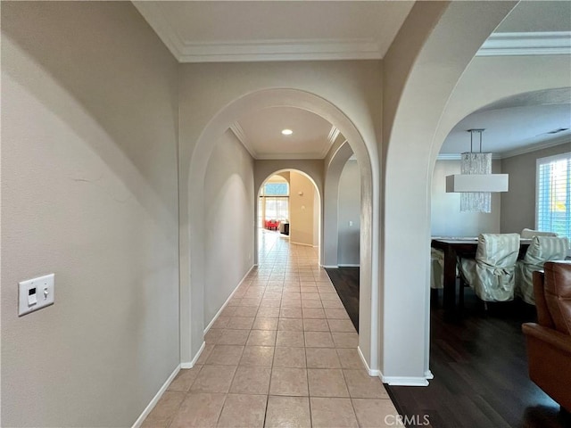 hallway with baseboards, ornamental molding, arched walkways, and light tile patterned flooring