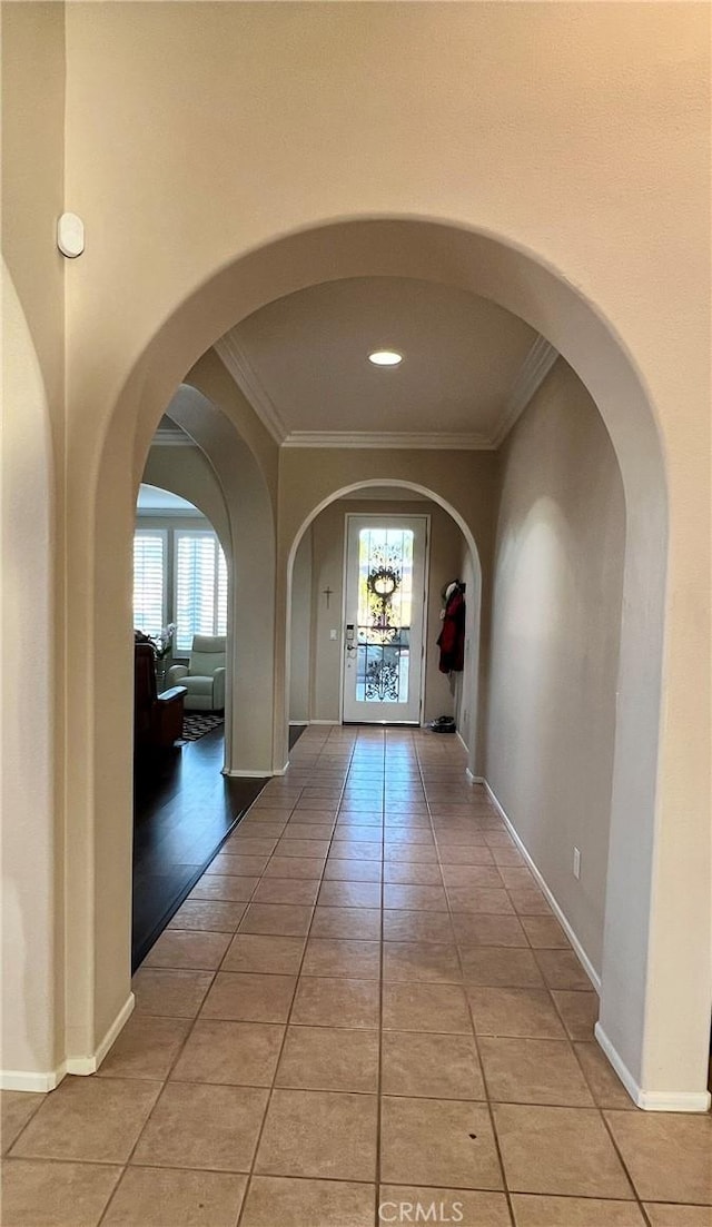 foyer featuring baseboards, ornamental molding, arched walkways, and tile patterned floors