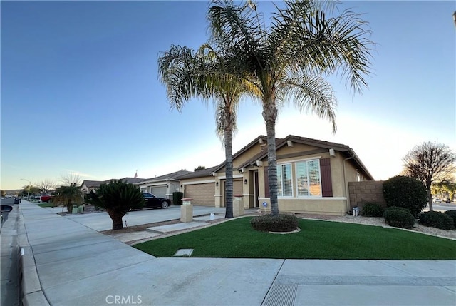 view of front of property featuring driveway, a garage, fence, a front lawn, and stucco siding