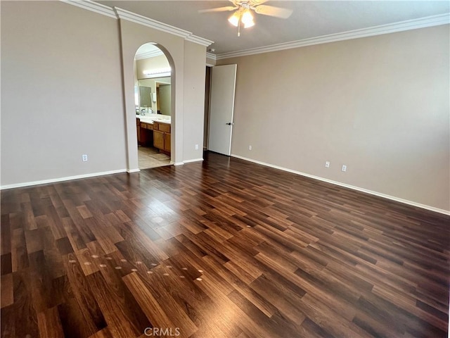 spare room with arched walkways, crown molding, dark wood-type flooring, a ceiling fan, and baseboards