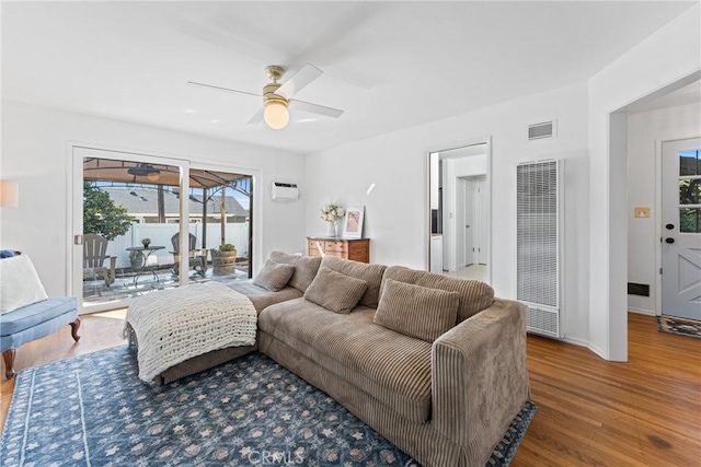 living area with wood finished floors, visible vents, baseboards, a ceiling fan, and a heating unit