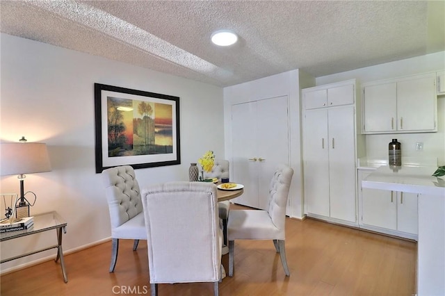 dining space featuring a textured ceiling, light wood-type flooring, and baseboards