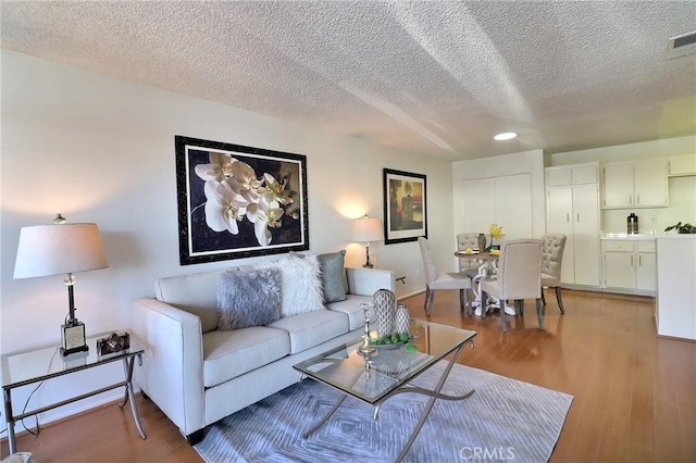 living area featuring a textured ceiling, visible vents, light wood-style flooring, and baseboards