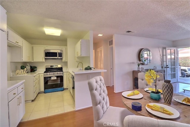 kitchen with appliances with stainless steel finishes, light countertops, visible vents, and white cabinetry