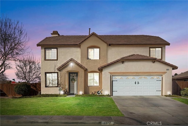 traditional-style house featuring stucco siding, fence, a garage, driveway, and a front lawn