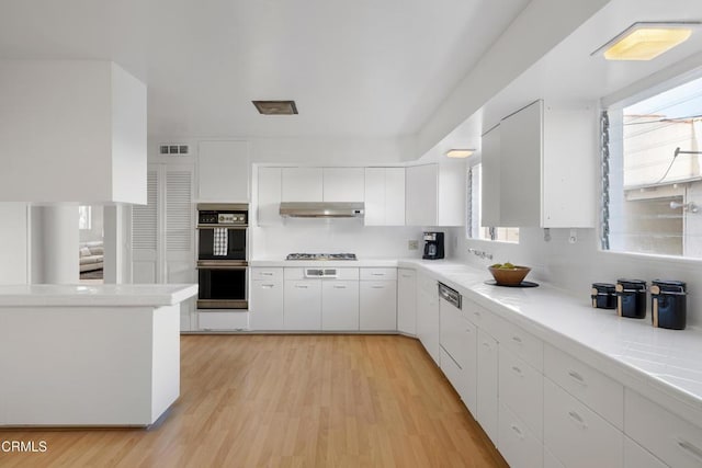 kitchen with dobule oven black, white cabinets, light countertops, under cabinet range hood, and stainless steel gas stovetop