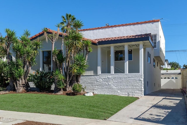 mediterranean / spanish-style house with stone siding, a front yard, a tile roof, and stucco siding