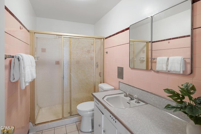 bathroom with toilet, tile patterned flooring, vanity, a shower stall, and tile walls