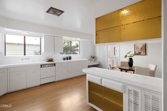 kitchen featuring tile countertops, light wood-style flooring, white dishwasher, white cabinetry, and a sink