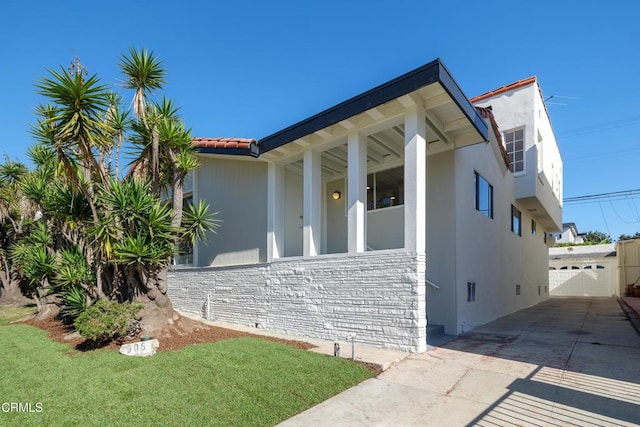 view of side of property featuring a garage, stone siding, a lawn, and stucco siding