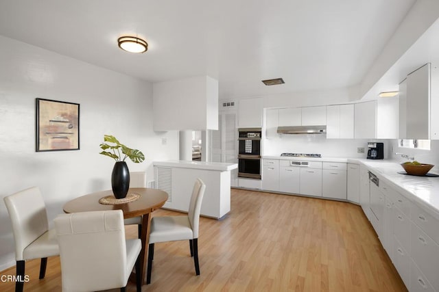 kitchen with tasteful backsplash, white cabinets, light wood-style flooring, light countertops, and under cabinet range hood