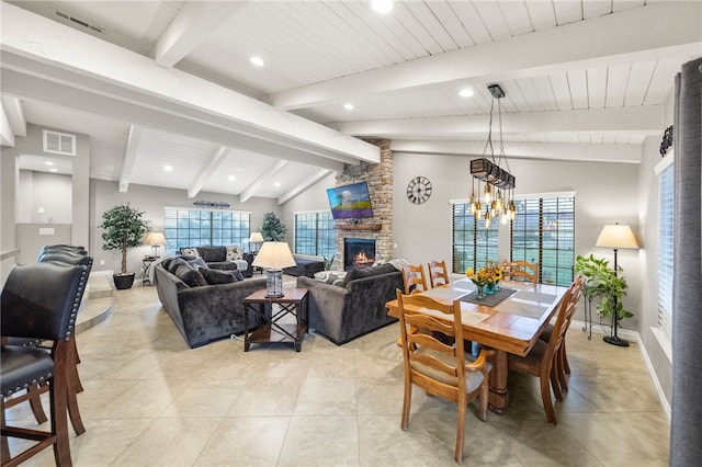 dining room featuring visible vents, baseboards, a stone fireplace, and vaulted ceiling with beams