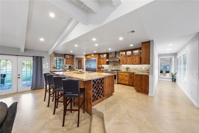 kitchen featuring visible vents, backsplash, brown cabinets, high end appliances, and wall chimney exhaust hood