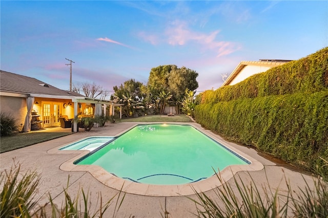 pool at dusk with french doors, a pool with connected hot tub, and a patio area