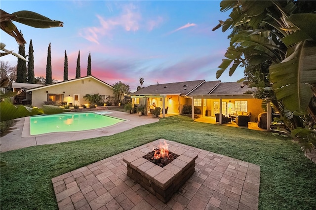 pool at dusk featuring an outdoor pool, a patio, a lawn, and an outdoor living space with a fire pit