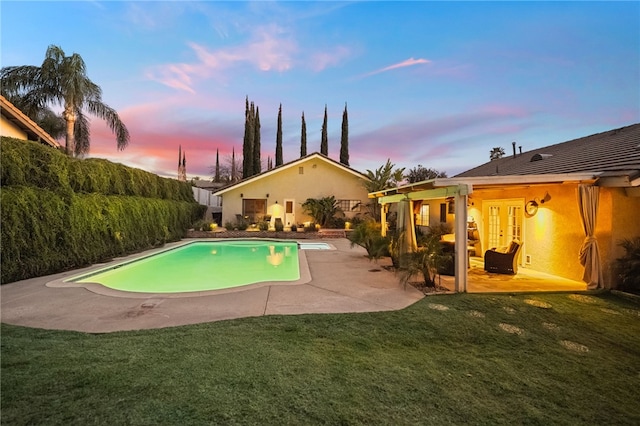 pool at dusk featuring a patio area, an outdoor pool, french doors, and a yard