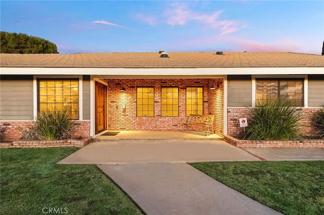 entrance to property featuring brick siding and a lawn