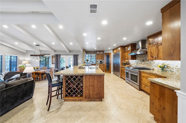 kitchen featuring brown cabinetry, visible vents, decorative backsplash, wall chimney range hood, and premium appliances