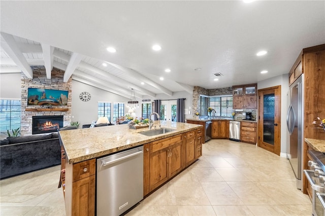 kitchen with a center island with sink, lofted ceiling with beams, premium appliances, brown cabinets, and a sink