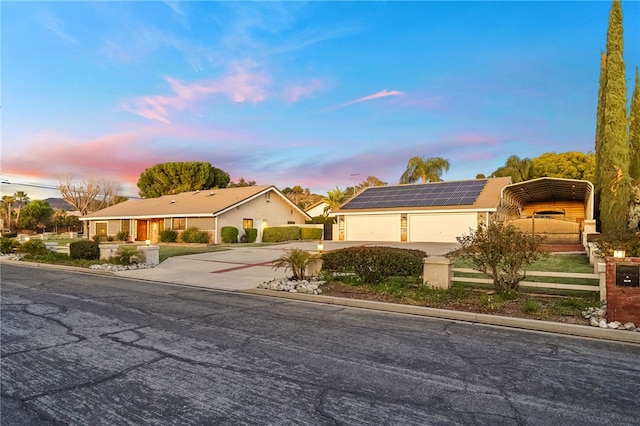 ranch-style home with roof mounted solar panels, a carport, concrete driveway, and fence