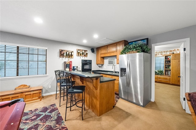 kitchen with a sink, black oven, dark countertops, stainless steel fridge, and a peninsula