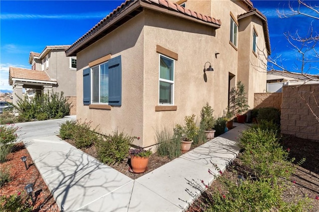 view of side of property featuring a tile roof, fence, a patio, and stucco siding