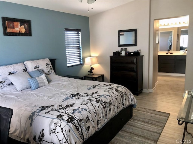 bedroom with light wood-type flooring, ensuite bath, baseboards, and a sink