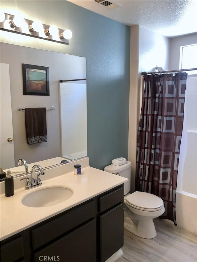 full bathroom featuring toilet, wood finished floors, shower / bath combination with curtain, vanity, and a textured ceiling