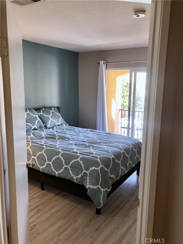 bedroom featuring access to outside, visible vents, a textured ceiling, and wood finished floors