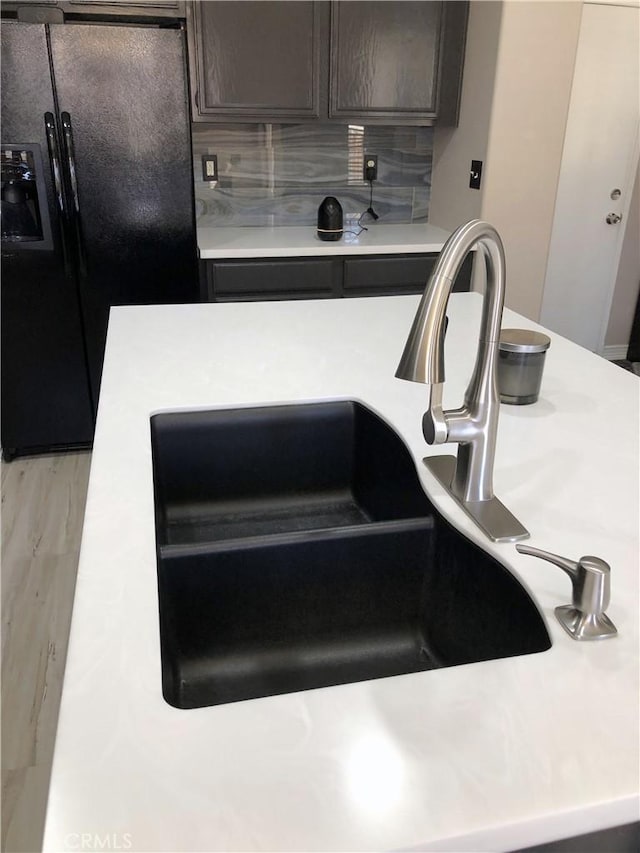 details featuring tasteful backsplash, light countertops, black refrigerator with ice dispenser, and a sink