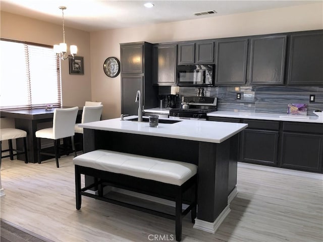 kitchen featuring a sink, light countertops, black appliances, pendant lighting, and backsplash