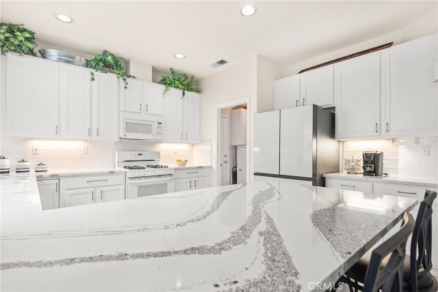 kitchen with decorative backsplash, white appliances, light stone counters, and white cabinetry