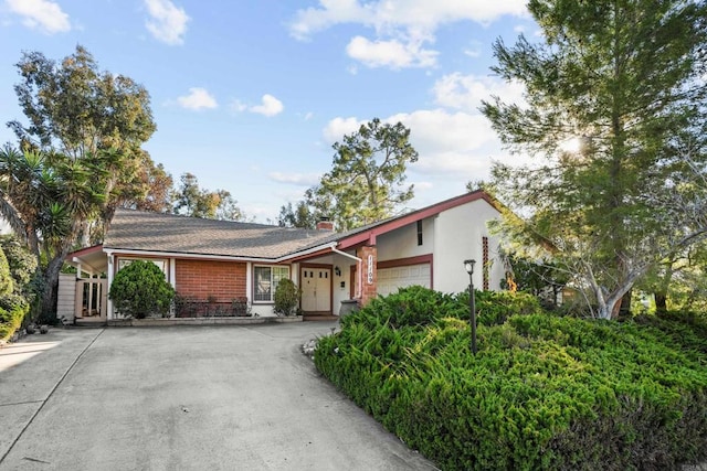 view of front of property featuring brick siding, a chimney, stucco siding, an attached garage, and driveway