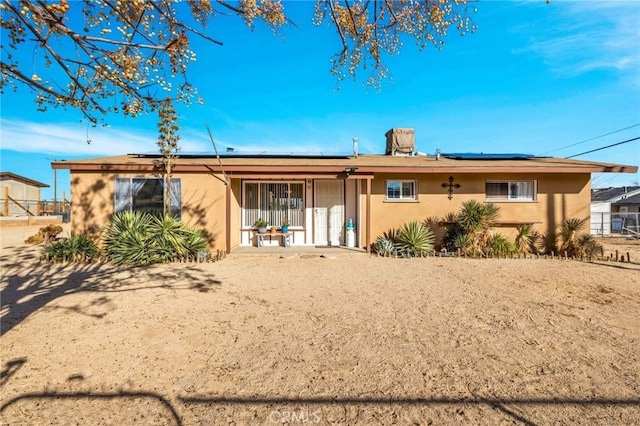 rear view of house with solar panels and stucco siding