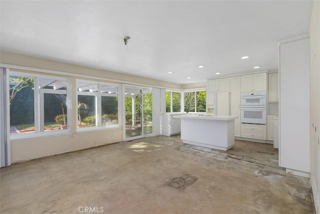 interior space with double oven, white cabinets, light countertops, a center island, and unfinished concrete floors