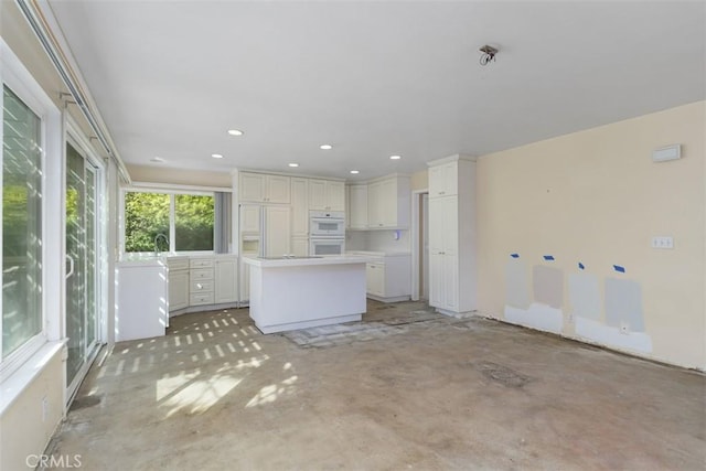 kitchen featuring concrete flooring, double oven, a kitchen island, white cabinetry, and light countertops